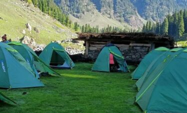 Camping tents in lush green valley during Kashmir Great Lakes Trek with Himalayan mountains