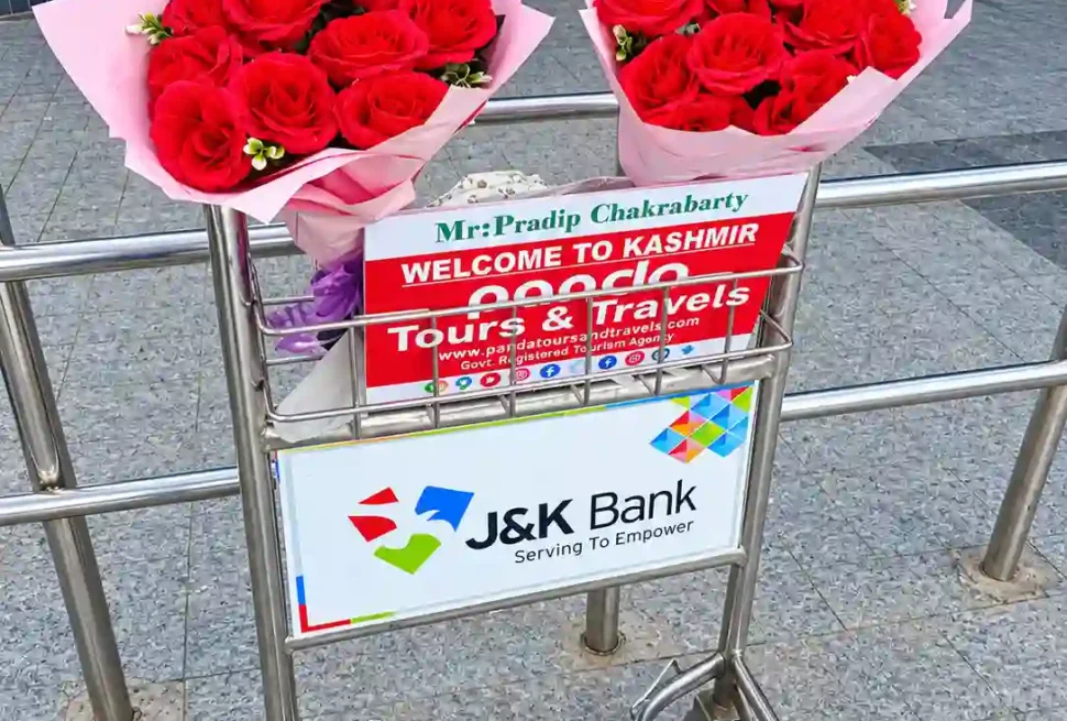 Panda Tours and Travels welcome board and red rose bouquets on a luggage trolley at Srinagar Airport