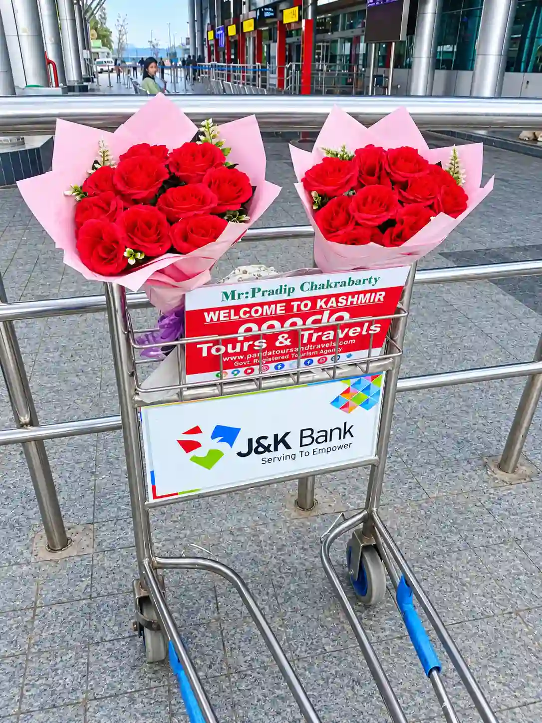 Panda Tours and Travels welcome board and red rose bouquets on a luggage trolley at Srinagar Airport